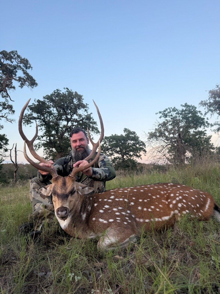 Bearded hunter smiling proudly holding wide antlers of trophy Axis buck