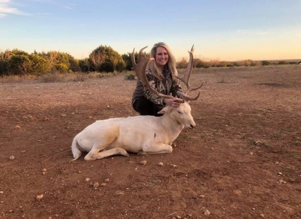 Huntress smiling beside trophy white Fallow Deer stag at golden hour sunset