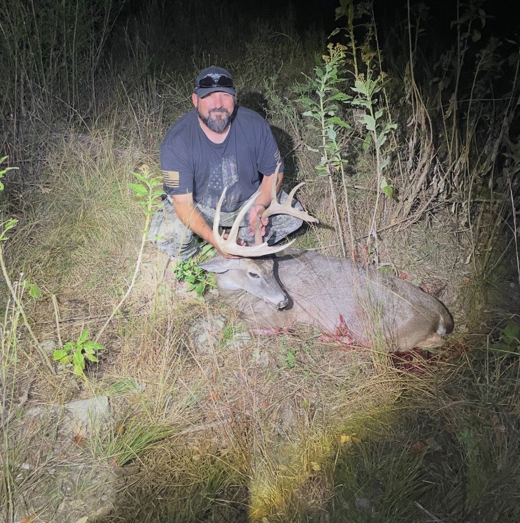 Hunter resting beside heavy-horned native white-tailed deer buck during evening harvest
