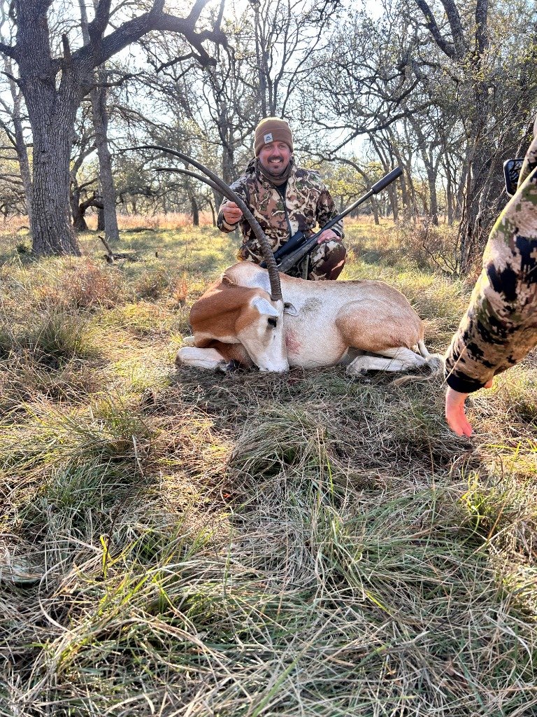Hunter kneeling beside trophy Scimitar Oryx with precision rifle