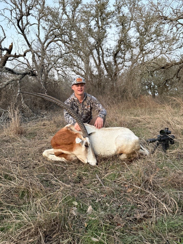 Young hunter smiling beside trophy Scimitar-horned Oryx in brush country