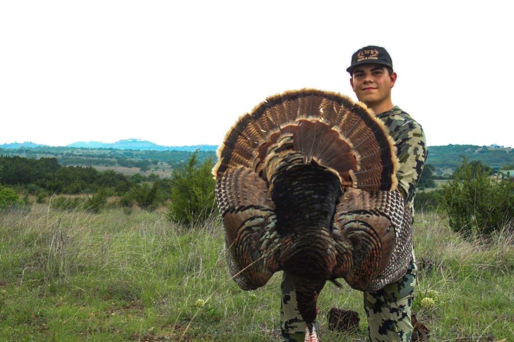 Hunter wearing LWE cap holding full Rio Grande turkey fan in Texas Hill Country